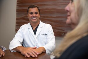 Dr. Clark sitting across from his patient, talking to her about how her smile can benefit from single and multiple dental implants.