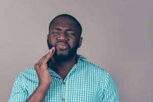 Photo of a dental patient holding his mouth in the spot of his troubled wisdom teeth